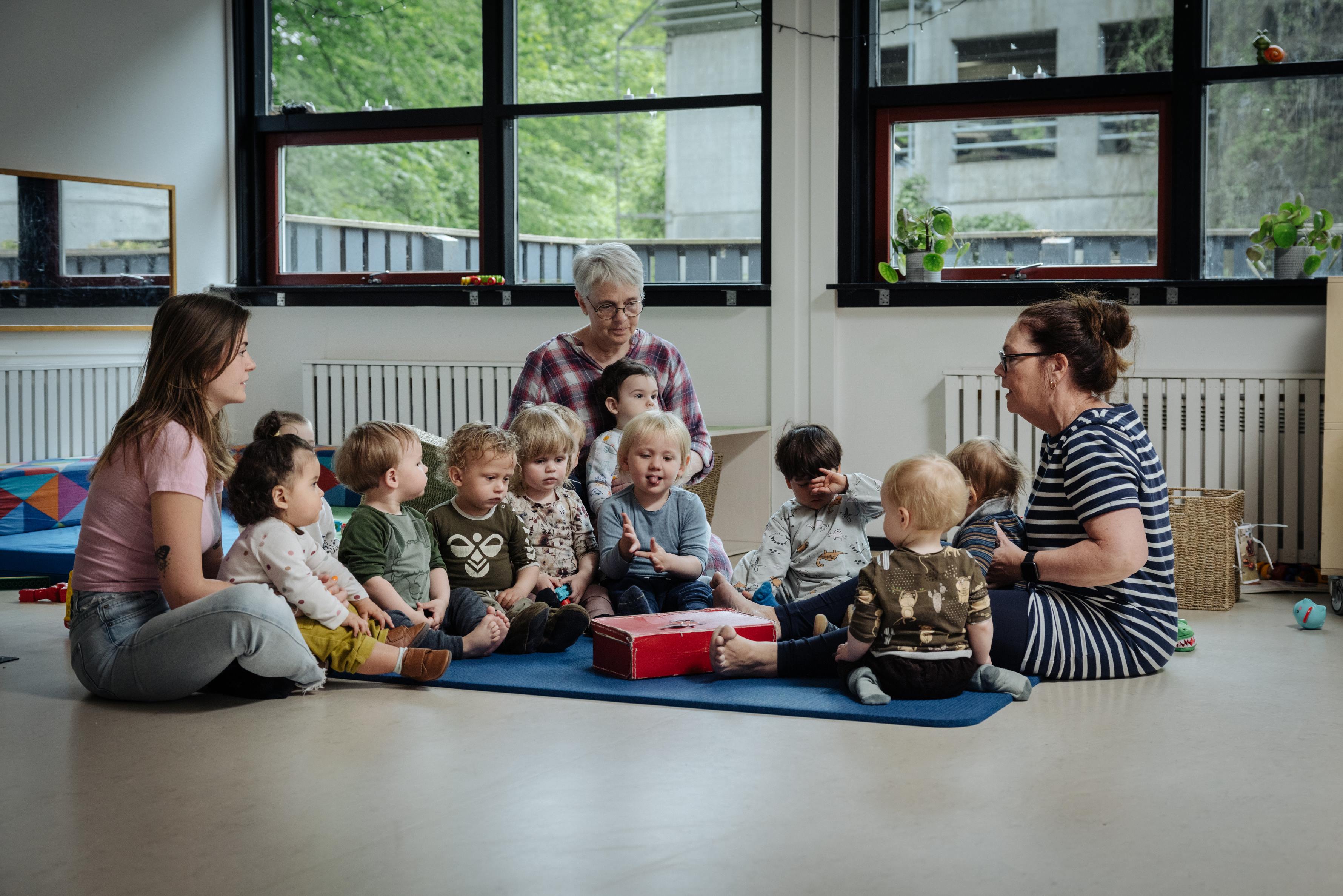 Børn og voksne sidder på gulvet til samling i daginstitutionen Trip Trap Træsko